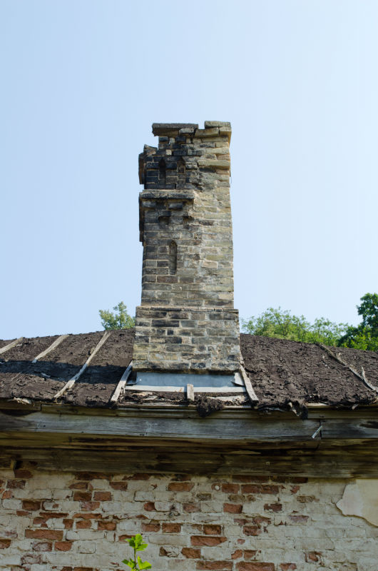 crumbling chimney sitting atop a deteriorating roof